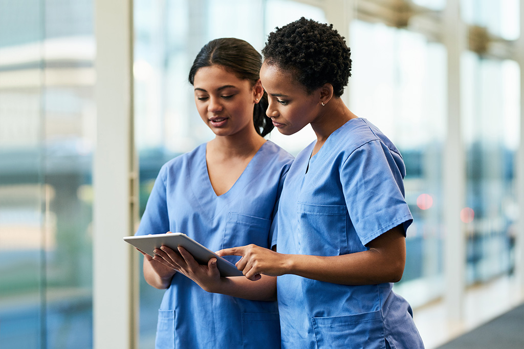 Two female medical practitioners using a digital tablet together in a hospital.