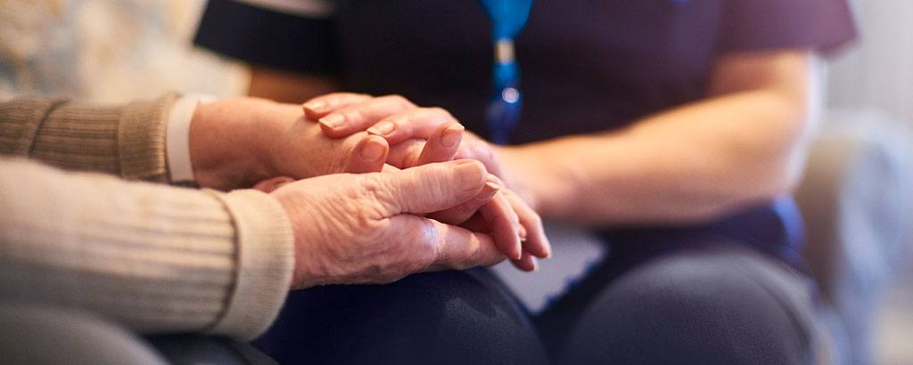 A caregiver holds an elderly patient's hand
