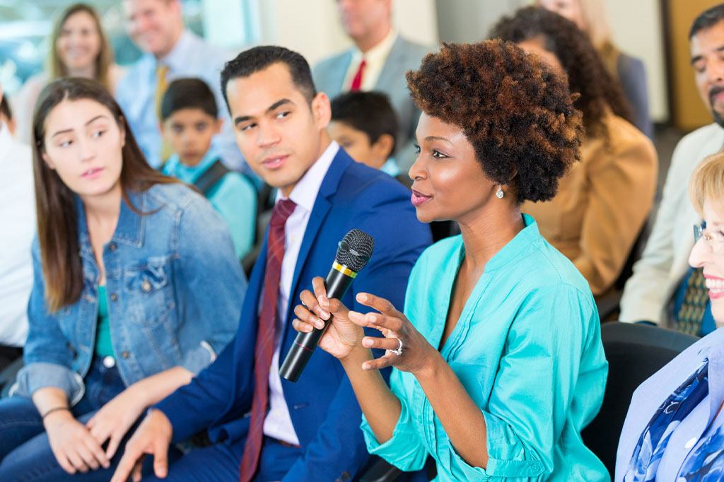 A woman with a microphone speaks at a professional engagement